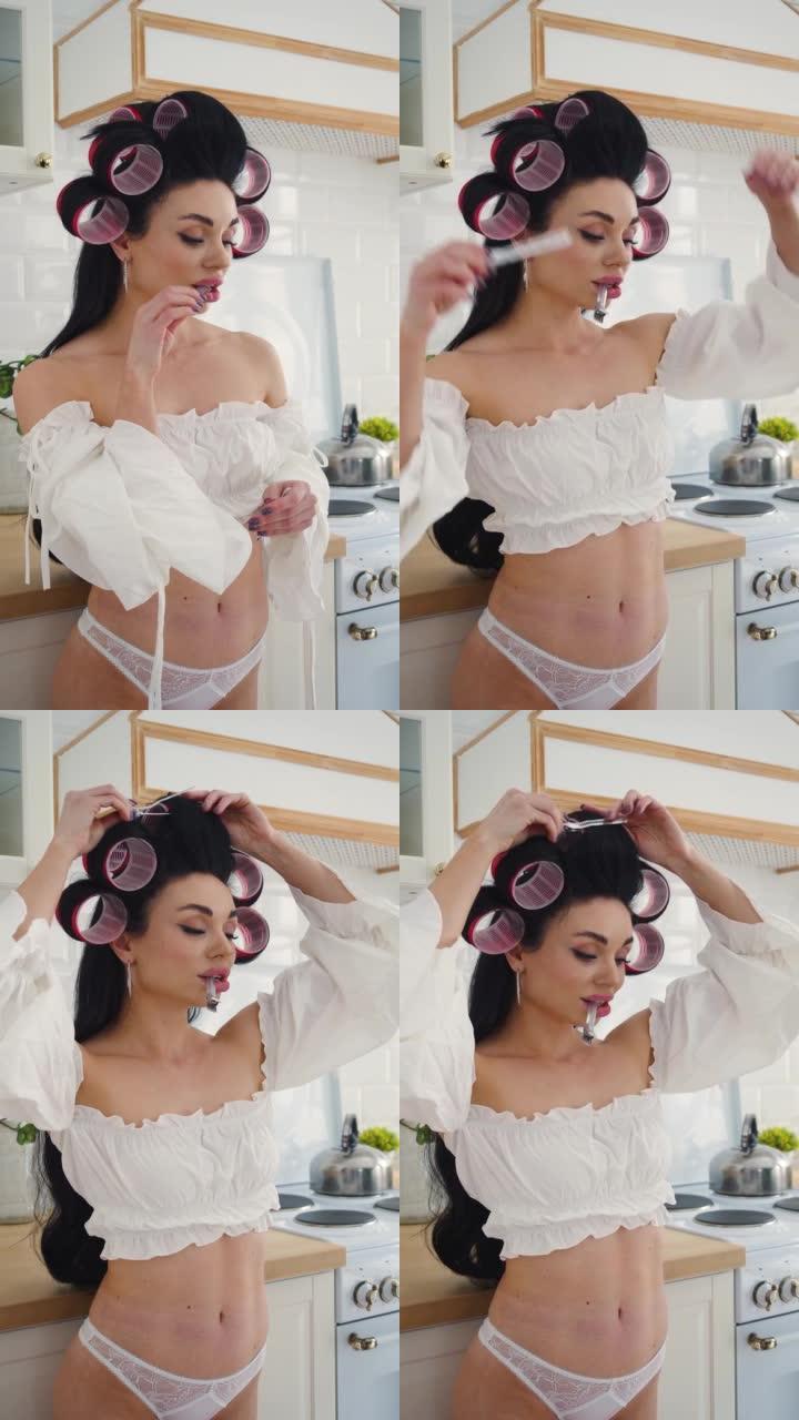 性感的35岁黑发女人在白色内衣站在厨房和插入发夹到她的头发。垂直镜头