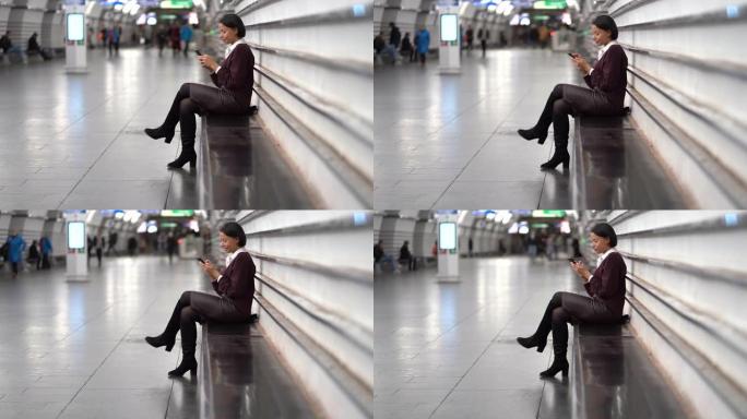 非洲女商人坐在地铁站站台上等待使用智能手机的火车
