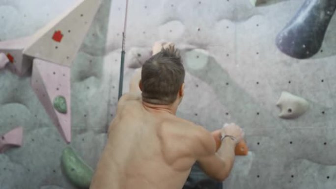 健壮的男性攀登者快速地爬上人造的攀岩墙。速度提升。一个强壮的有经验的攀岩者在里面练习爬圆石墙