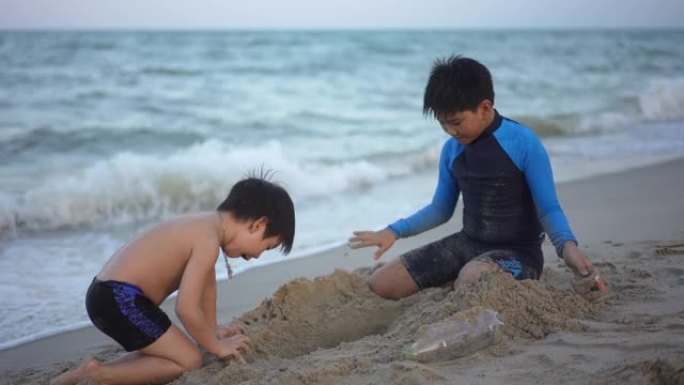 亚洲男孩兄弟在日落时在海滩上享受和玩海和沙子