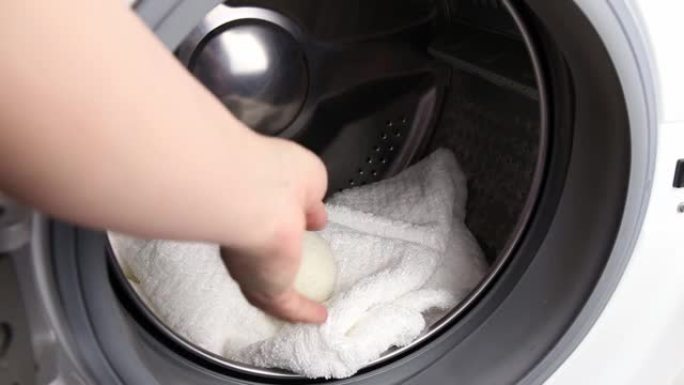 女人在洗衣机概念中使用羊毛烘干机球做更柔软的衣服，同时滚筒烘干。放电静电，缩短干燥时间，节约能源。