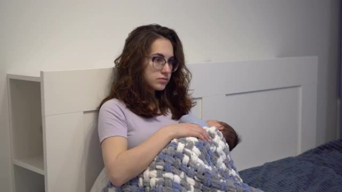一位精疲力竭的年轻母亲在床上抱着一个孩子。一个疯狂疲惫的女人，怀里抱着一个新生儿。