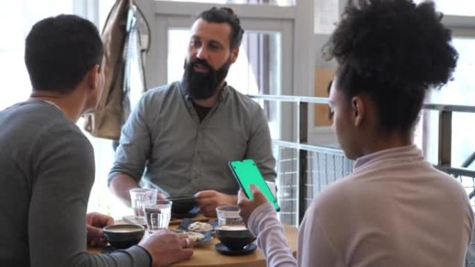 坐在咖啡馆里并使用移动应用程序付款的多样化朋友