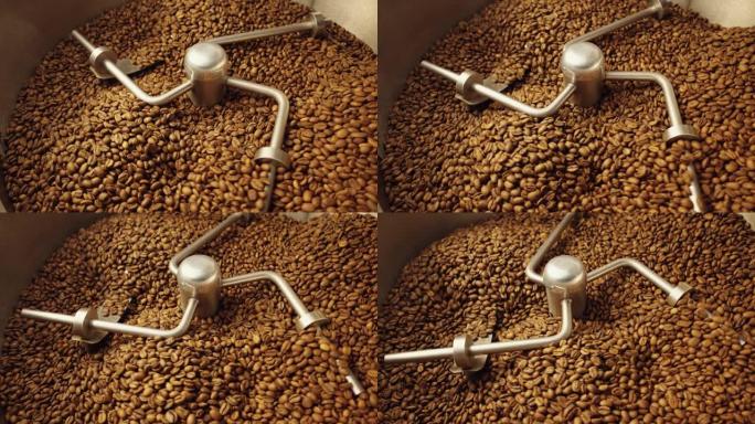 生产新鲜烘焙的咖啡豆。工业混合机在焙烧炉中混合烘焙咖啡豆，特写镜头。工厂烘烤过程。咖啡馆的餐饮背景。