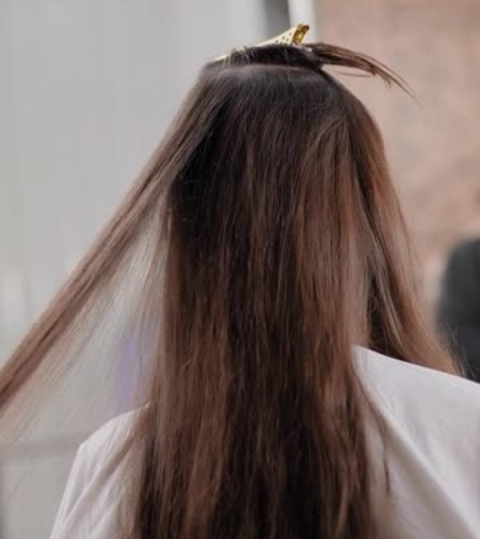 理发师的特写镜头正在使用吹风机烘干女性客户的长发，使发廊在高光和剪发后头发变直。