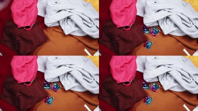 在五颜六色的衣服上扔洗涤凝胶荚，洗衣机用洗涤剂胶囊。洗衣概念，去污剂和化学清洁剂，液体肥皂