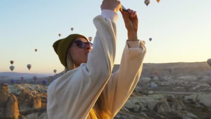 土耳其卡帕多西亚-2019年11月: 年轻女性用苹果手机给气球拍照