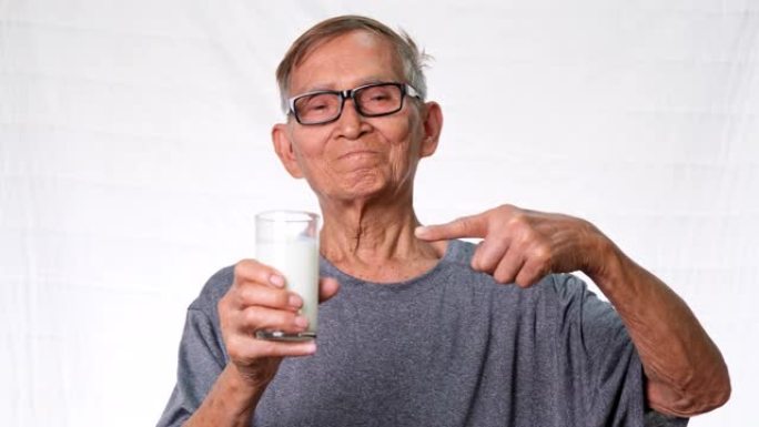 在工作室里，健康的老人拿着一杯牛奶指着白色背景上的玻璃杯。