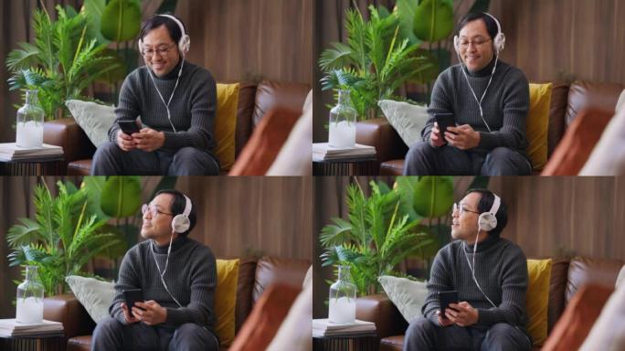 蛤蜊和安静的在家开朗的亚洲年轻男性带着耳机和智能手机播放列表选择在家里的客厅在智能手机上播放歌曲