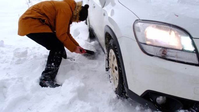 男子用汽车铲子在雪地里挖出失速的汽车。冬天的运输在降雪后被困在雪堆中，坐在底部。急救，拖车，冬季轮胎