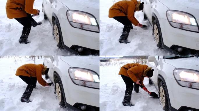 男子用汽车铲子在雪地里挖出失速的汽车。冬天的运输在降雪后被困在雪堆中，坐在底部。急救，拖车，冬季轮胎