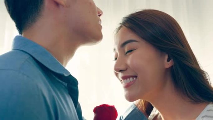 亚洲年轻人惊喜并将玫瑰花送给美丽的女友。迷人的浪漫新婚夫妇男女花时间在家里一起庆祝周年纪念日和情人节