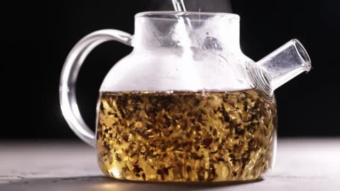 在深色背景下的玻璃透明茶壶中酿造红茶的过程。将热水倒入带茶叶的水壶中。