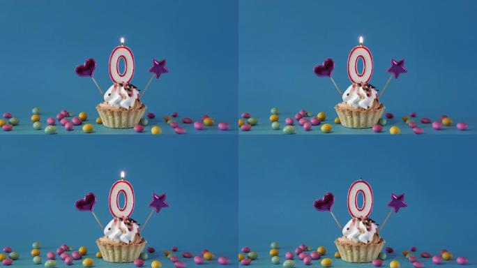 给0岁的孩子生日快乐，带蜡烛的生日蛋糕和蓝色背景上的生日装饰品。点燃并熄灭纸杯蛋糕上的节日蜡烛