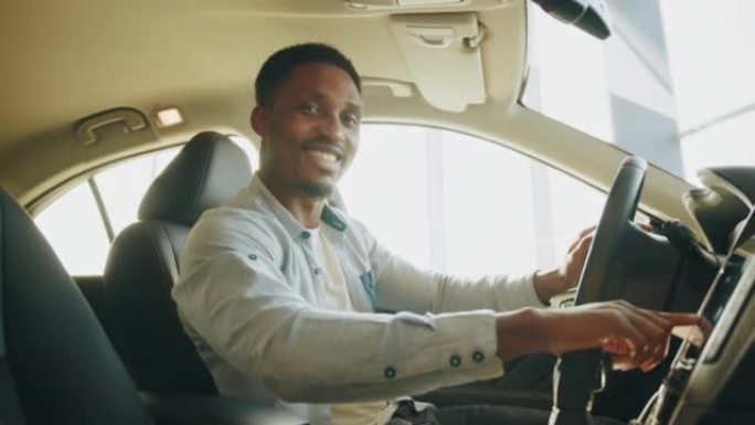 一个人测试一辆新车。专注的非洲男子坐在驾驶座上，使用仪表板进行导航的侧视图。男子按下汽车多媒体面板上