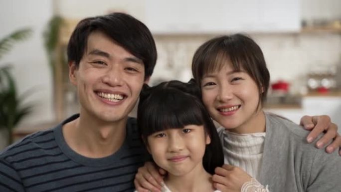 美丽的亚洲三口之家互相拥抱，在家微笑着看着相机的头像。