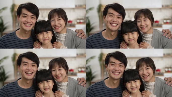 美丽的亚洲三口之家互相拥抱，在家微笑着看着相机的头像。