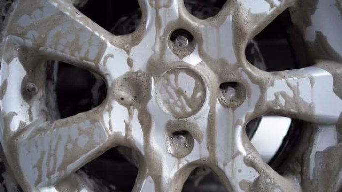 轮胎轮辋车轮和轮胎的洗车特写。现代用高压水洗车。精致的无接触洗车用肥皂泡沫。大量肮脏的滴水泡沫
