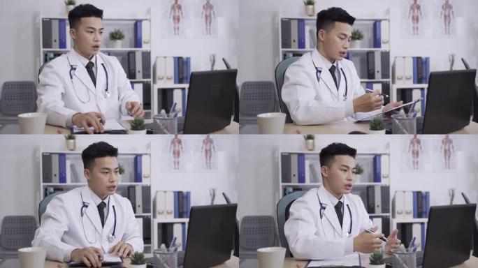 亚洲医务人员正在与患者的文件和手势交谈，同时在医院的办公桌上的笔记本电脑上进行虚拟医生的访问，远程医