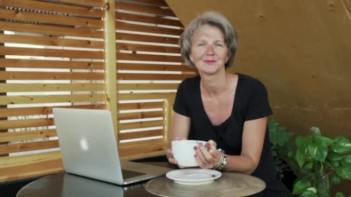 英俊的白发女士在咖啡馆用笔记本电脑在相机里看的肖像