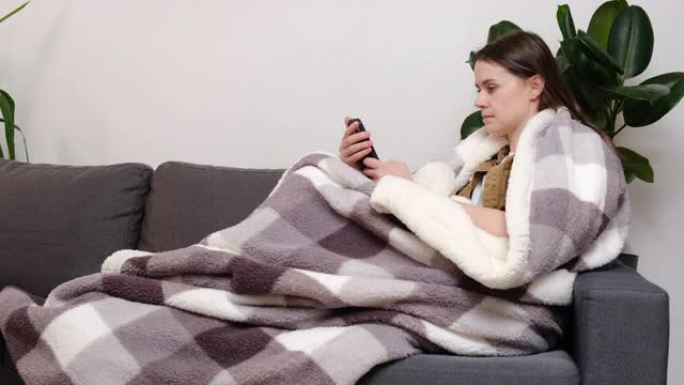 阅读良好的媒体新闻概念。迷人的年轻女子穿着格子，坐在舒适的沙发上，配有智能手机，在互联网上购买电子商