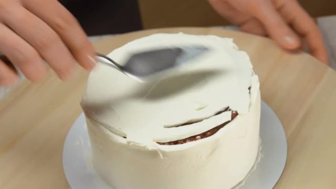 厨房用抹刀将甜奶油抹平在红色天鹅绒蛋糕上