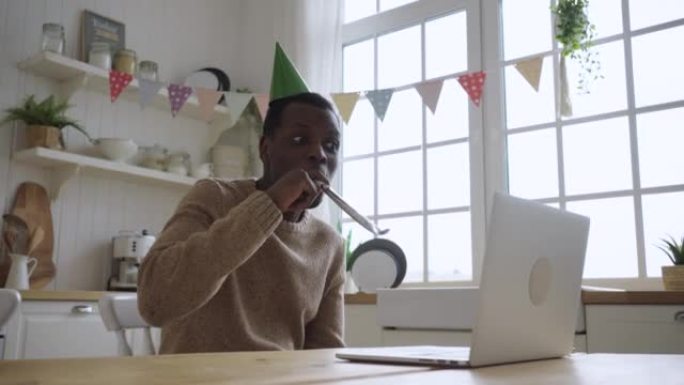 戴着绿色帽子的快乐黑人男子在笔记本电脑上通过视频电话在线祝朋友生日快乐