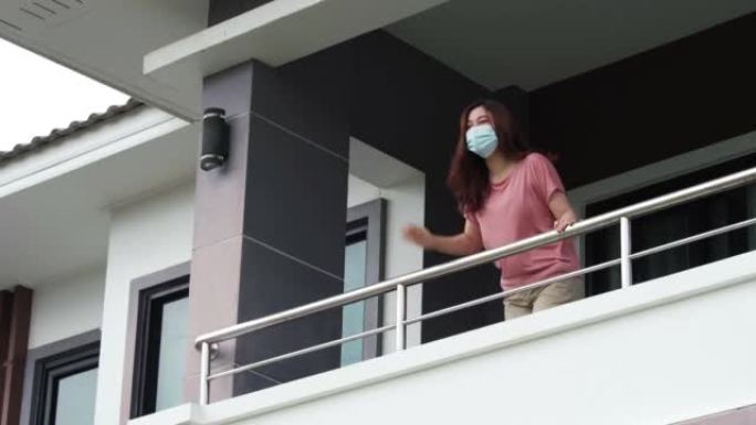 检疫妇女戴着口罩，在家里的阳台上与邻居打招呼，下雨，冠状病毒 (新型冠状病毒肺炎) 大流行