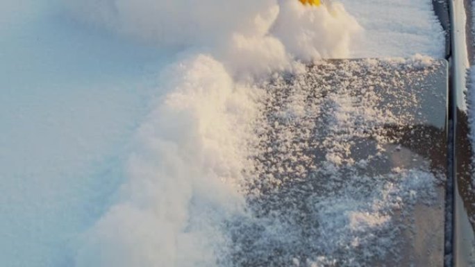 汽车清洁冰雪的特写镜头。冬天降雪后用刷子清理汽车挡风玻璃上的雪。冬天开车前的繁忙工作日