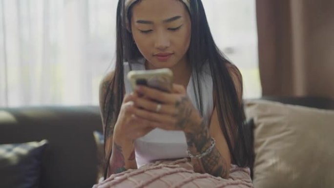 年轻亚洲女性在家中使用智能手机的肖像。