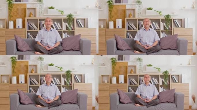 成熟的亚洲男子在家做瑜伽冥想在客厅的瑜伽垫上。老年或老年男子蛤蜊冥想深呼吸，在舒适的家中放松。快乐退