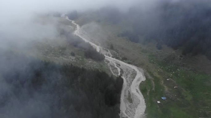 在阴天，有雾和低云，被绿色的高山森林包围的山区河流的鸟瞰图。神秘山谷4k的低空飞行概述