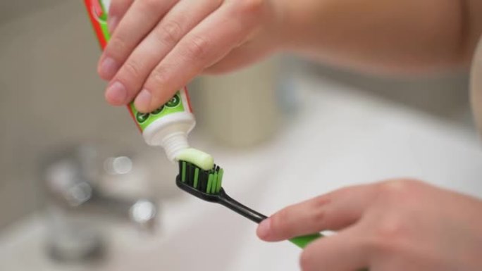 用手从黑色和绿色牙刷上的浴室水槽上的管子上挤压绿色牙膏。准备刷牙。牙科护理，习惯，日常生活
