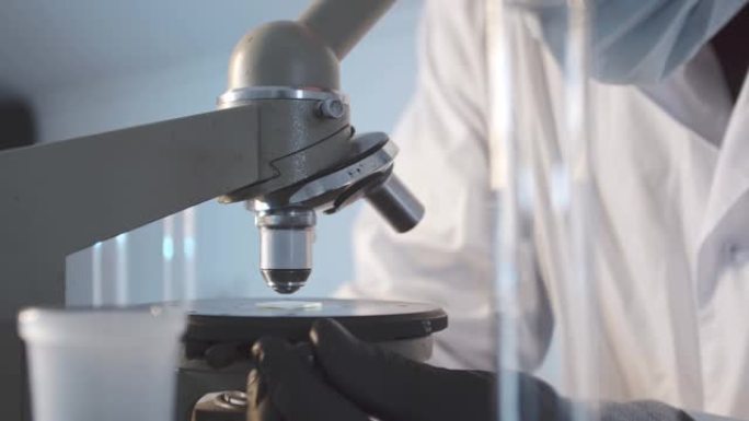 一个男人在实验室里的特写镜头在载玻片上安装了一个显微镜。在科学实验室进行研究工作。戴着防护橡胶手套的