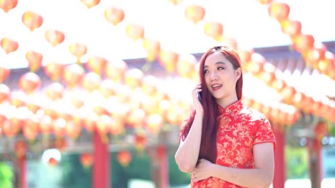 亚洲美女身穿红色中国传统旗袍，用手机装饰中国新年主题。