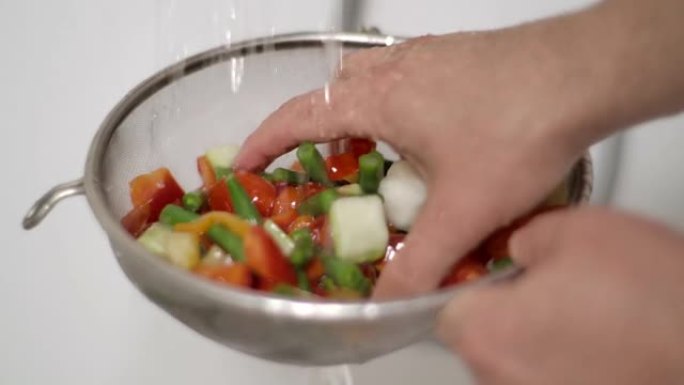 雄性手洗黄瓜辣椒粉番茄青豆玉米番茄辣椒花椰菜胡萝卜。用手慢动作用水清洗新鲜切碎的蔬菜。素食有机保健食