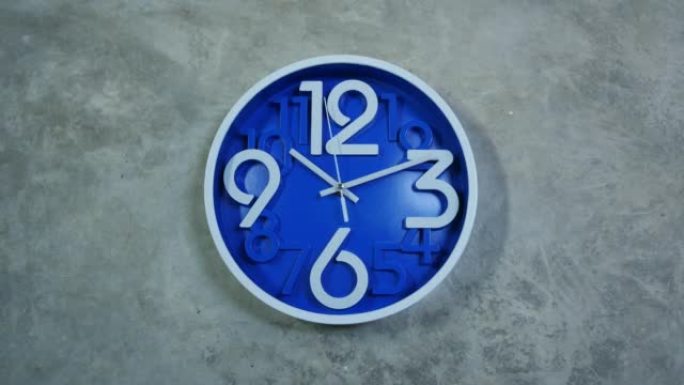 一个蓝色的办公室时钟挂在灰色的混凝土墙上。时间流逝