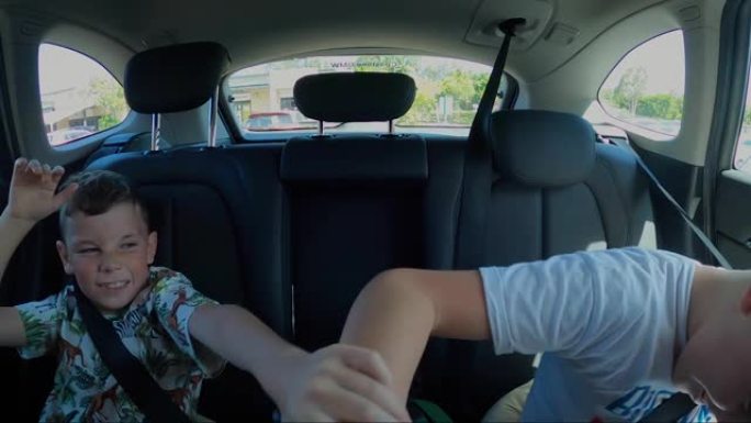 两个小子慢动作在汽车后座上打架。抬起手臂和双手，斜视和退缩。