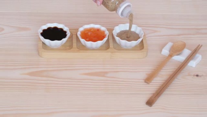 竹架上的白杯中的三种酱汁，木桌背景上的筷子和勺子。
