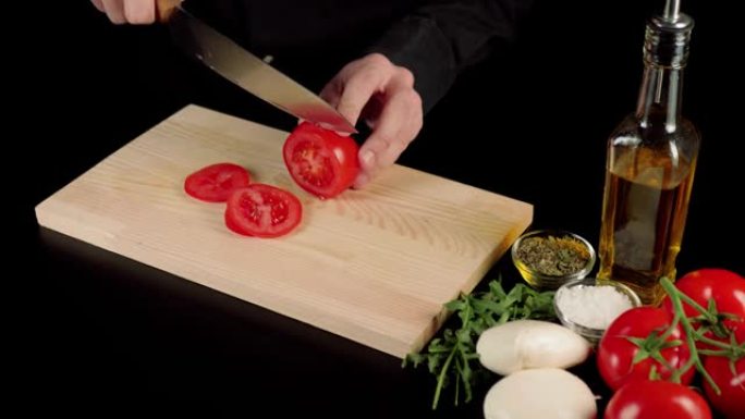 专业厨师在木板上切成新鲜多汁的红番茄。黑桌装饰有caprese沙拉成分-西红柿，马苏里拉奶酪，芝麻菜