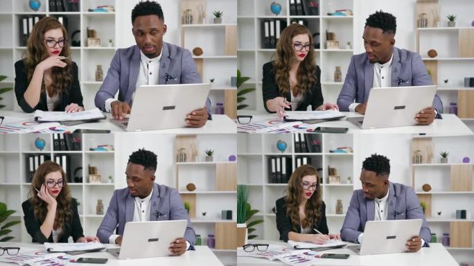 好看的昂扬自信的年轻女商人和黑皮肤的商人在现代办公室里用笔记本电脑和文件一起工作