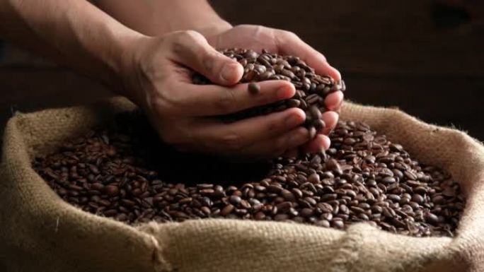 双手舀起烤咖啡豆。新鲜烘烤的芳香浓郁的深棕色咖啡豆在一大堆新鲜咖啡豆上sc起。慢动作。