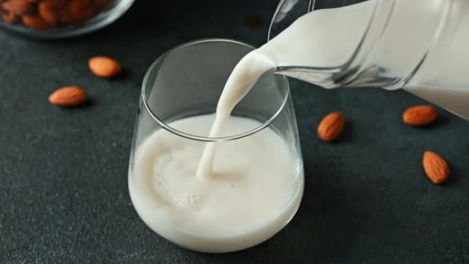 将杏仁奶倒入玻璃杯中。纯素食牛奶。植物性牛奶替代品和无乳糖。替代牛奶。将牛奶倒入玻璃杯中。