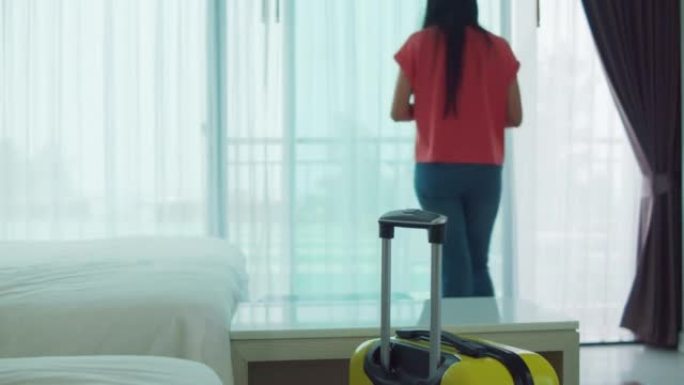 女人带着行李进入酒店房间，在房间里用智能手机打字。