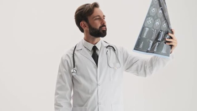 有吸引力的男人医生，听诊器微笑着，并在专心地看着x射线图像时表现出拇指向上的手势