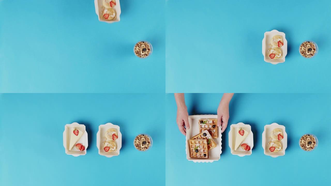 送餐顶视图，在蓝色背景上的一次性容器中带走甜点。午餐盒配有煮熟的芝士蛋糕、比利时华夫饼。餐饮糖果服务