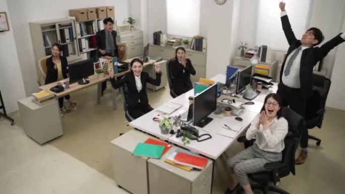 快乐公司团队的高角度镜头看着相机，用手在办公室鼓掌欢呼好商业新闻