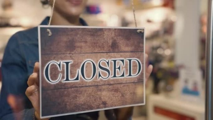 年轻的非洲裔美国妇女在购物中心的一家女装品牌服装店的门上从打开到关闭。服装店结束了工作日。特写。慢动
