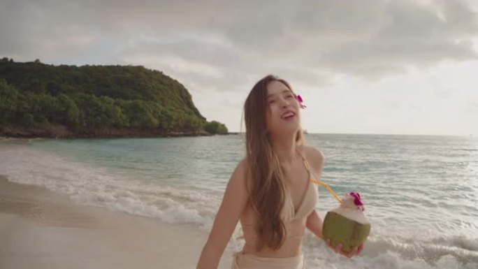 穿着泳衣的亚洲年轻女性，椰子水在沙滩上散步。