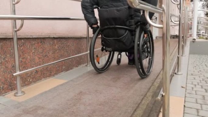 残疾人坐在轮椅上沿着街道移动，爬上坡道